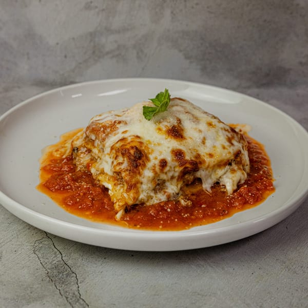 A serving of lasagna with melted cheese and tomato sauce, garnished with a mint leaf.