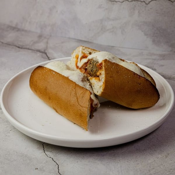 A meatball sub sandwich, cut in half, with melted cheese and sauce on a white plate.