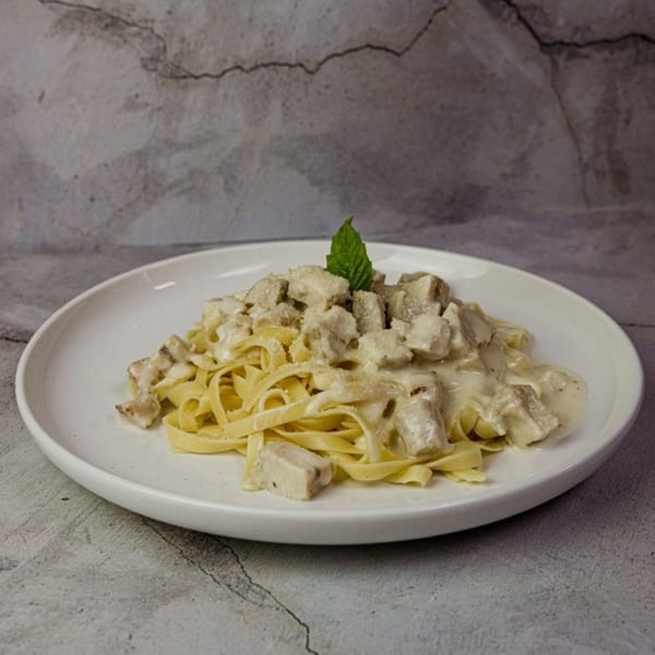 Creamy chicken fettuccine alfredo with a mint garnish on a white plate.