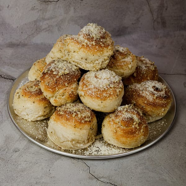 A metal tray piled high with golden-brown garlic knots, dusted with Parmesan cheese and herbs.