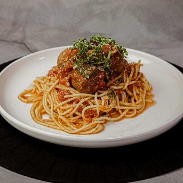 Spaghetti and meatballs with red sauce, parmesan, and fresh basil on a white plate.