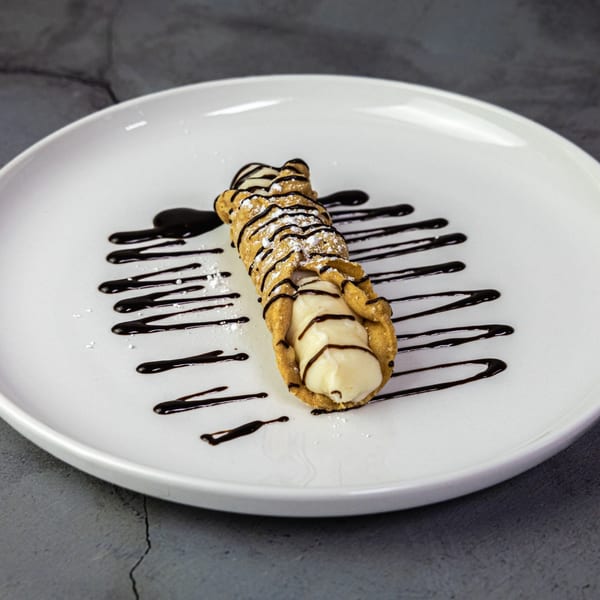 A cannoli drizzled with chocolate sauce and powdered sugar on a white plate.