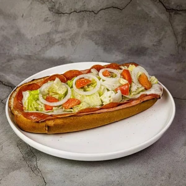 A pepperoni sub sandwich with lettuce, tomatoes, and onions on a white plate.